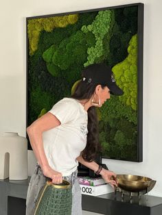 a woman standing in front of a painting holding a frying pan and looking at it