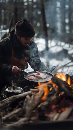 a man cooking food over an open fire in the woods on a cold winter day