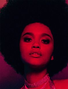 a woman with an afro wearing a necklace and choker in front of a red background