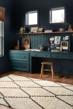 a room with two windows and a rug on the floor in front of an office desk