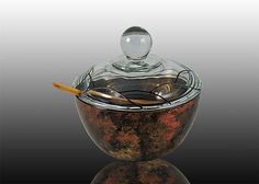 a glass bowl with a wooden spoon in it on a reflective surface and the lid is open