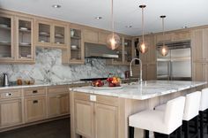 a large kitchen with marble counter tops and wooden cabinetry, along with white stools