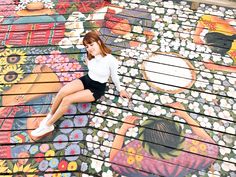 a young woman sitting on top of a wooden bench covered in flowers and butterflies painted on it