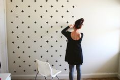 a woman standing in front of a wall with black crosses on it and her back to the camera