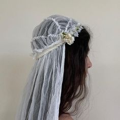 a woman wearing a veil with flowers on it's head and her hair in the wind