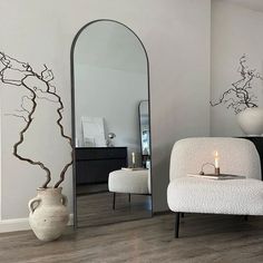 a white chair sitting in front of a mirror next to a vase and candle on a table