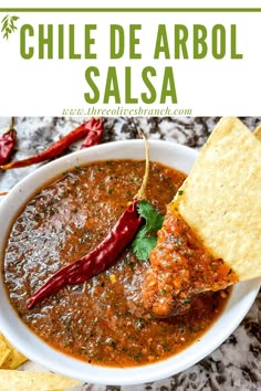 a white bowl filled with chili and salsa next to tortilla chips on the side