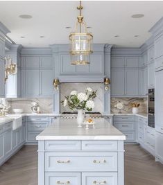 a large kitchen with blue cabinets and white counter tops, gold chandelier hanging from the ceiling