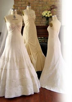 three wedding dresses on mannequins in front of a brick wall and fireplace