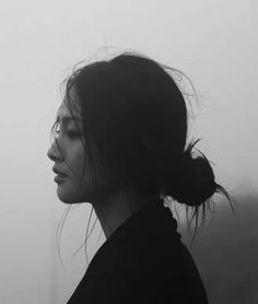 a black and white photo of a woman with her hair blowing in the wind on a foggy day