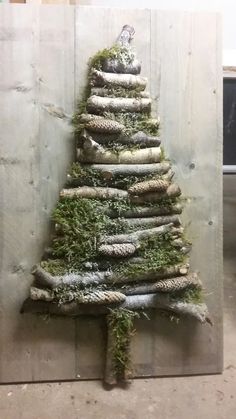 a christmas tree made out of branches and moss is displayed in front of a wall