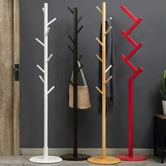 three coat racks are standing next to each other in front of a gray wall and a potted plant