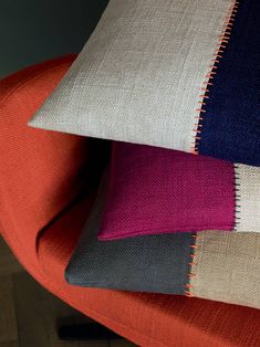 three different colored pillows stacked on top of each other in an orange, blue, and pink chair