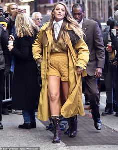 a woman walking down the street in short shorts and knee high boots, wearing a trench coat