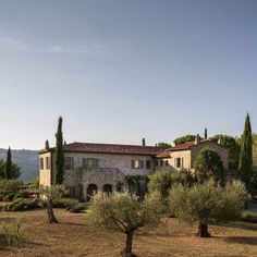 an old house surrounded by olive trees in the middle of a field with mountains in the background