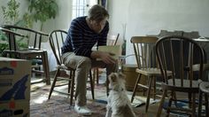 a man sitting at a table with a dog in front of him and looking at something on the floor