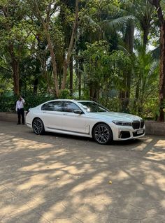 a man standing next to a white car parked in front of some trees and bushes