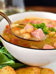 a spoon full of soup with ham and broccoli in it next to crackers