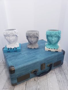 three ceramic busturines sitting on top of an old blue piece of luggage,