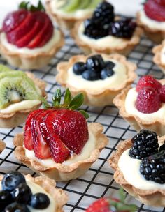 some fruit tarts are sitting on a cooling rack with berries and kiwis