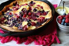 a pancake with berries and blueberries in it next to a bowl of strawberries