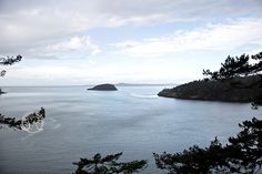 the water is calm and blue with some clouds in the sky above it, as seen from an overlook point on a cloudy day