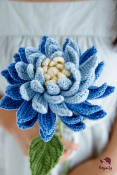 a crocheted blue and white flower is held by a woman's hand