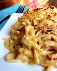 a white plate topped with macaroni and cheese covered in sauce next to a fork