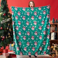 a woman is holding up a green christmas blanket with snowflakes and santa's faces on it