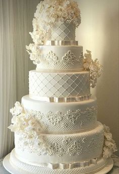 a white wedding cake with flowers on the top and bottom tiers is displayed in front of a window