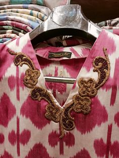 a pink and white shirt with an ornate design on the collar is hanging from a rack