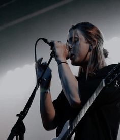 a woman with makeup on her face singing into a microphone while holding a guitar in front of her