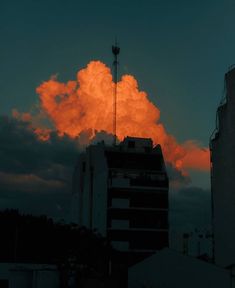 an orange cloud is in the sky above some tall buildings and a building with a television antenna on top