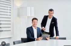 two men are sitting at a table and one is holding a tablet while the other man looks on