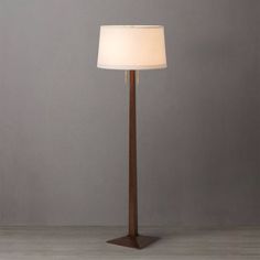 a floor lamp with a white shade on it's side and a wooden base