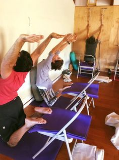 two men doing yoga exercises on blue mats in a room with wooden floors and walls