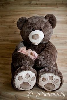 a large teddy bear sitting on top of a wooden floor next to a sleeping baby