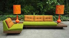 a green couch sitting next to two orange lamps on top of a wooden table in front of trees