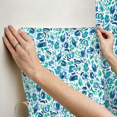 a woman is painting a wall with blue and green flowers on it, while another person holds the edge of her hand