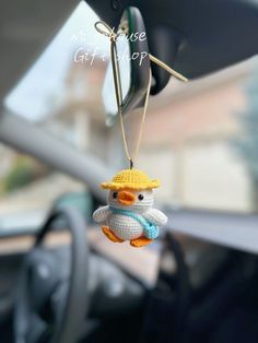 a small stuffed bird hanging from the dashboard of a car with a yellow hat on it's head