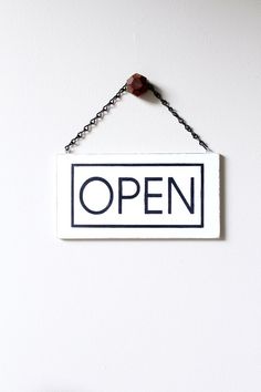 an open sign hanging from a chain on the wall next to a potted plant