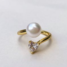 a pearl and gold ring on a white surface with a single diamond in the middle