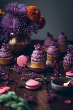 cupcakes with purple frosting and flowers in the background on a wooden table