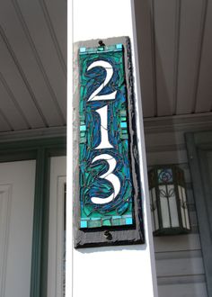 a house number sign hanging from the side of a white building with blue and green paint