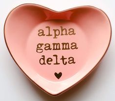 a pink heart shaped dish with the words alpha gama delta written on it