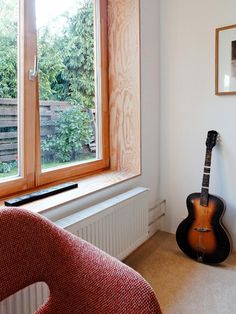 a guitar sitting in front of a window next to a chair and radiator