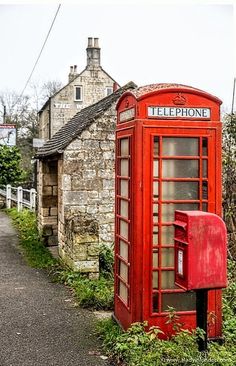 a red phone booth sitting on the side of a road next to a stone building