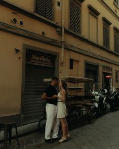 a man and woman kissing in front of a motorcycle parked on the side of a street