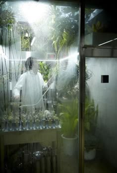 a man standing in front of a glass door surrounded by plants and water hoses