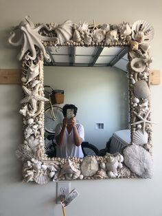 a person taking a selfie in front of a mirror with seashells on it